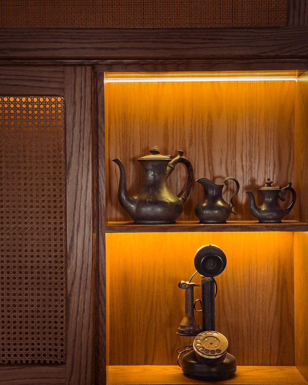 A wood niche with vintage teapots and a candlestick telephone, lit amber
